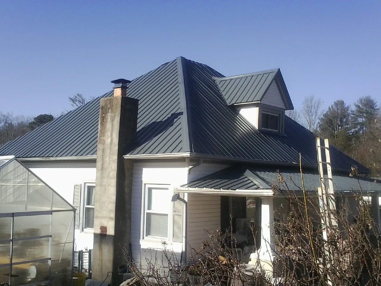 Dark blue standing seam metal roof on a white farmhouse with dormer — Slate & Tile Roof Repair by Roofing Brothers in Windfall