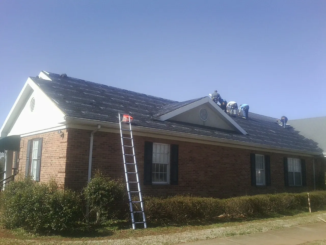Crew tearing shingles off a brick ranch roof with a ladder set — Emergency Roof Repair work by our crew in Windfall