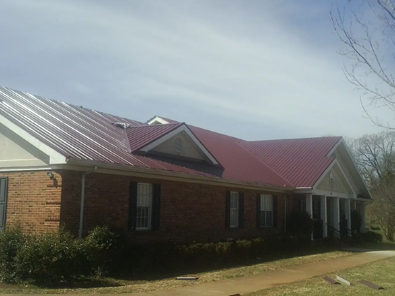 Red metal roof with gabled entries on a long brick building, from a Hail Damage Roof Repair job in Windfall