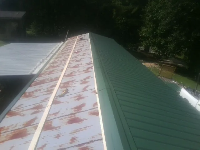Old rusted panels beside newly installed green metal roofing — Wind Damage Roof Repair by Roofing Brothers in Windfall