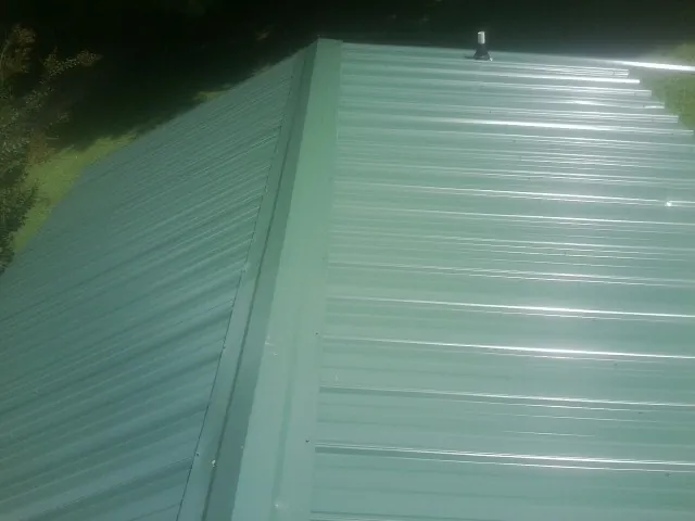 New green metal panels meeting at the ridge of a roof — Flat Roof Repair work by our crew in Windfall
