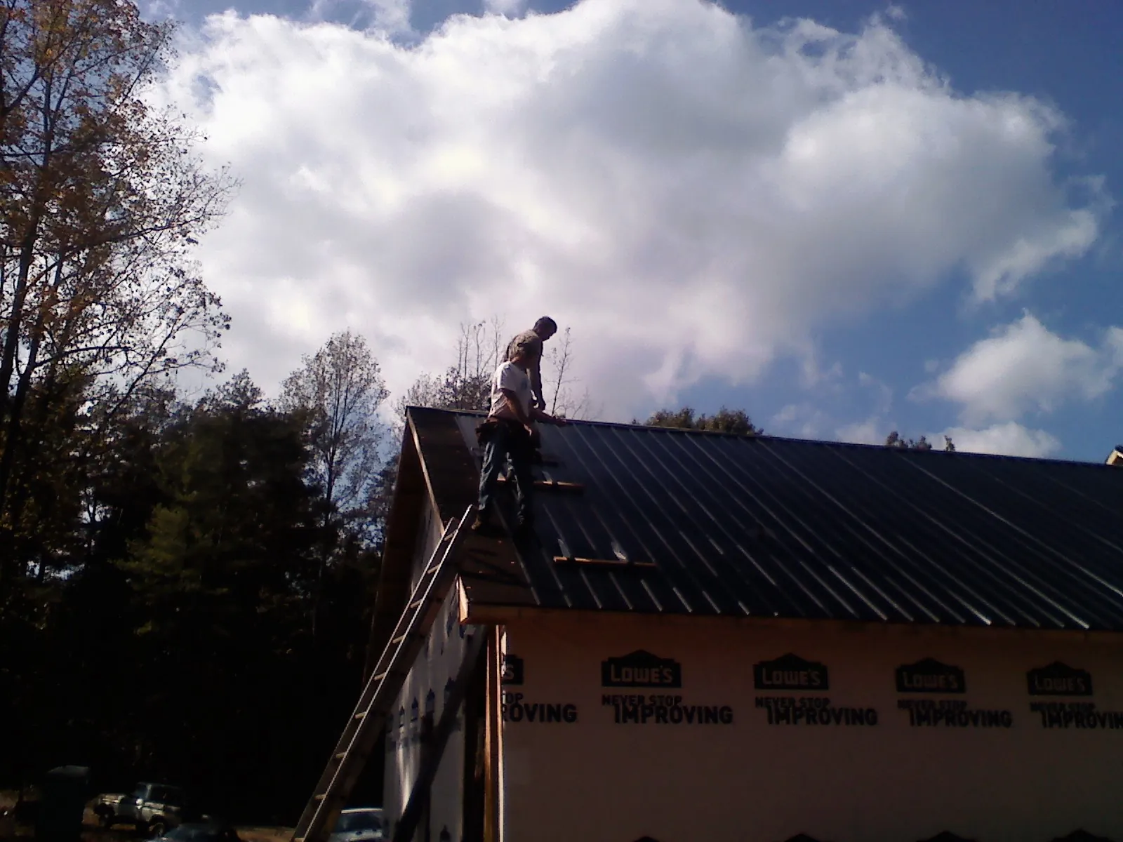 Roofer fastening dark metal panels high against a cloudy sky, from a Roof Inspection job in Windfall